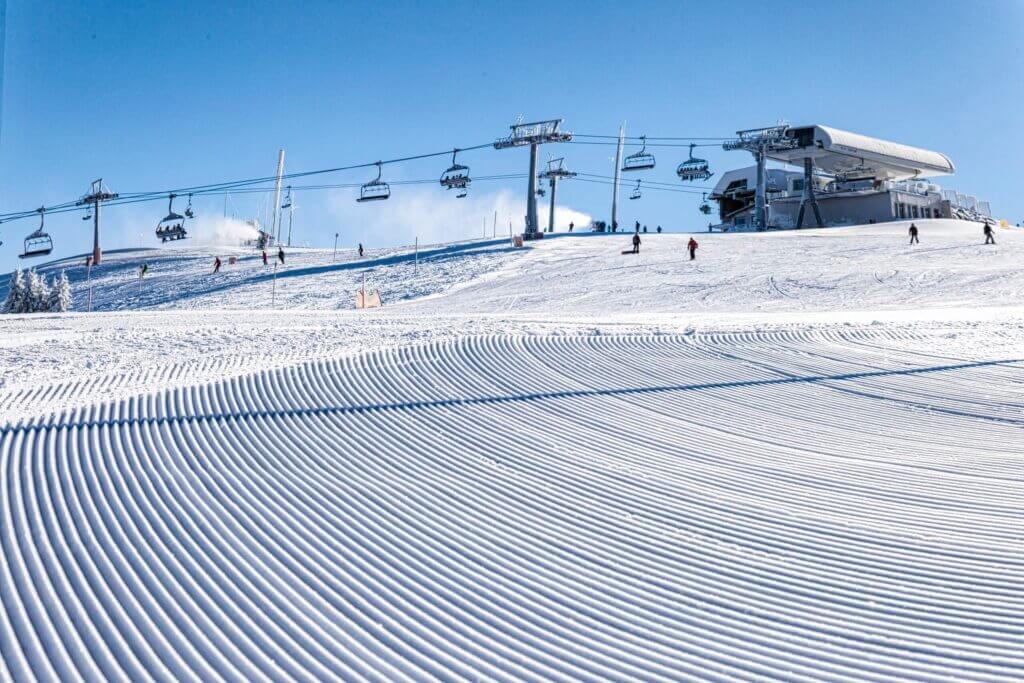 Perfekt präparierte Skipiste mit Sessellift und Skifahrern bei strahlend blauem Himmel. Optimal für Wintersportler.