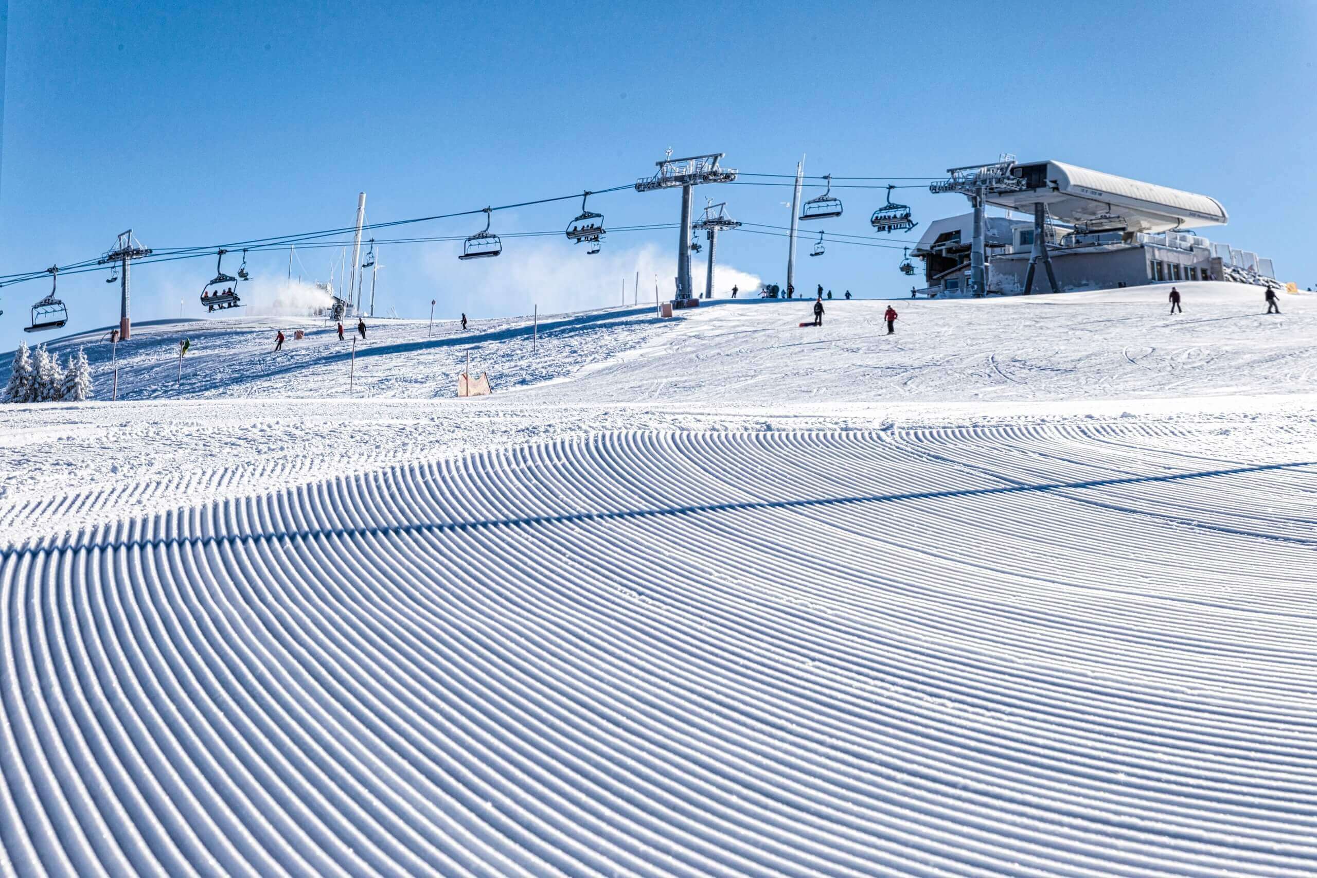 Perfekt präparierte Skipiste mit Sessellift und Skifahrern bei strahlend blauem Himmel. Optimal für Wintersportler.
