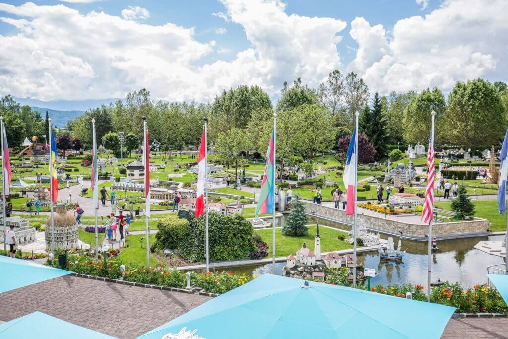 Miniaturpark mit internationalen Flaggen und Besuchern bei sonnigem Wetter, eingebettet in grüne Landschaft.