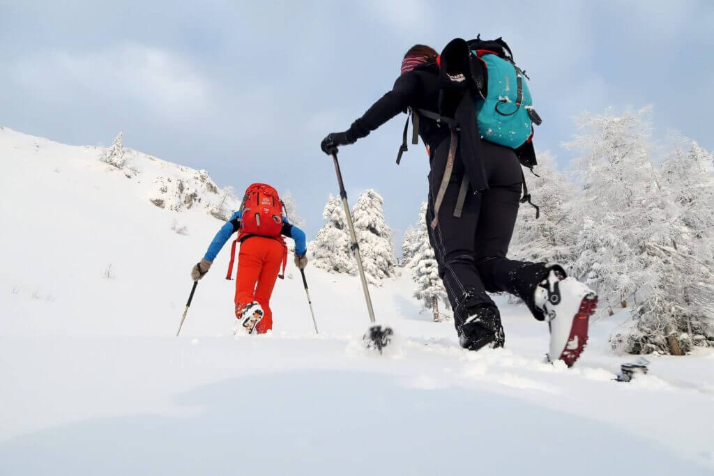 Zwei Bergsteiger mit Schneeschuhen erklimmen einen winterlichen Hang bei strahlend blauem Himmel.