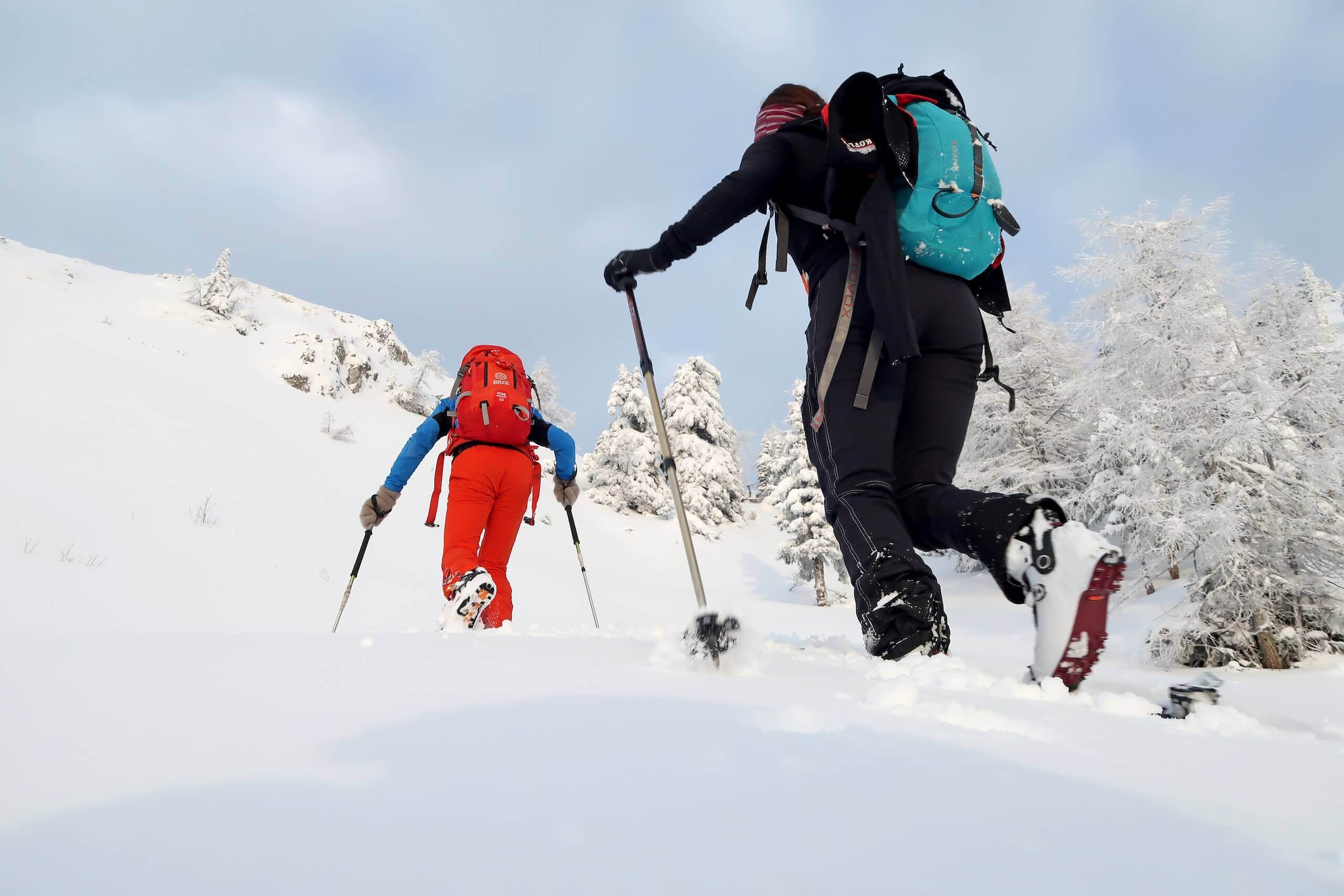 Zwei Bergsteiger mit Schneeschuhen erklimmen einen winterlichen Hang bei strahlend blauem Himmel.