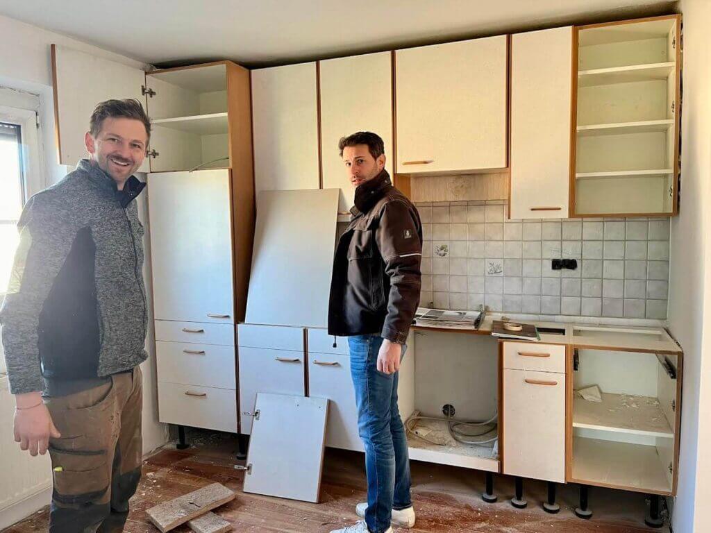 Zwei Handwerker renovieren eine Küche, leere Schränke und abgenommene Türen, Planung der Küchengestaltung.