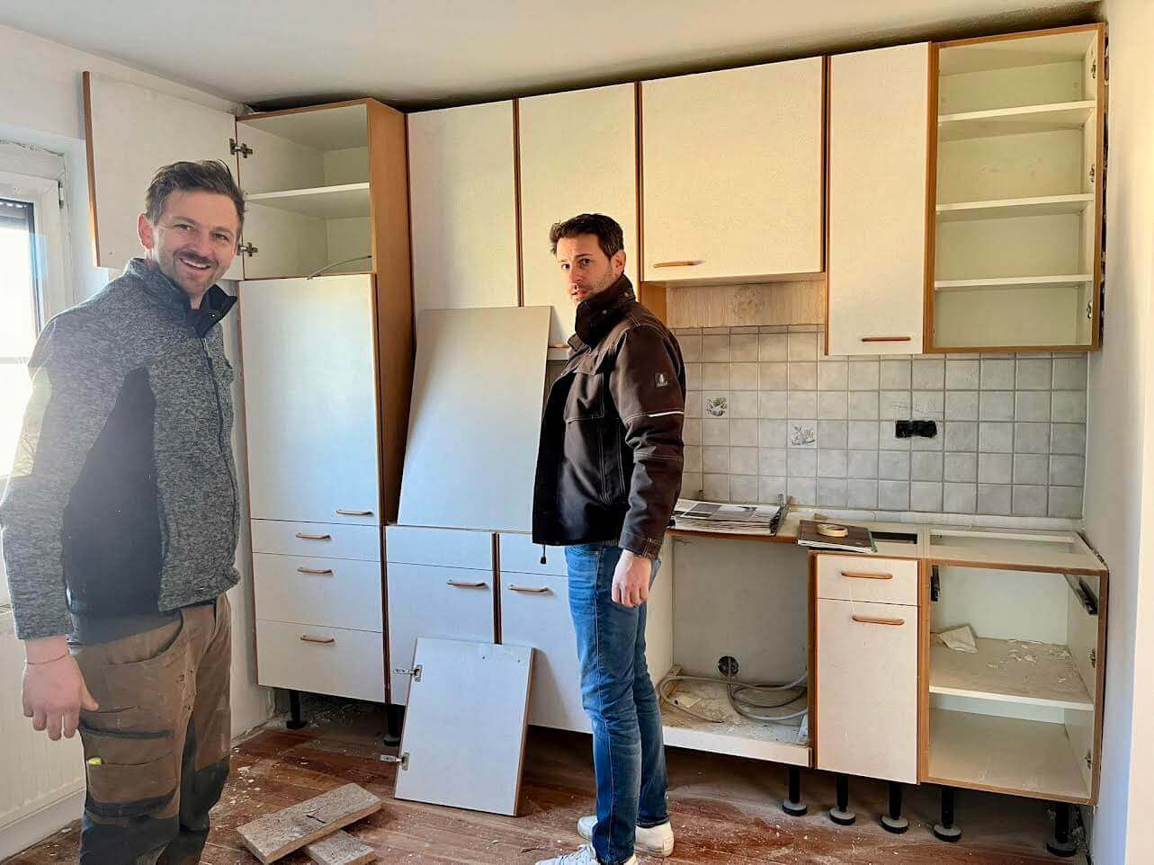 Zwei Handwerker renovieren eine Küche, leere Schränke und abgenommene Türen, Planung der Küchengestaltung.
