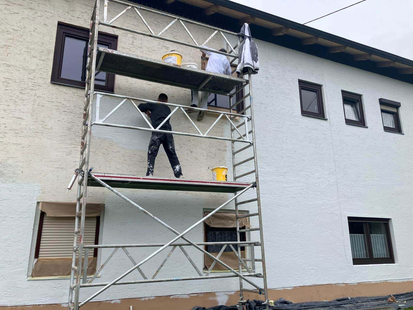 Malerarbeiten an einem Haus: Zwei Handwerker auf Gerüst streichen die Fassade weiß.