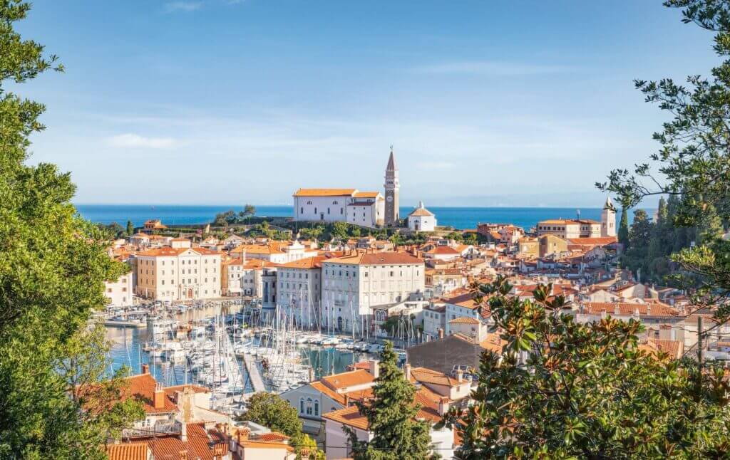 Panorama von Piran, Slowenien mit malerischem Hafen, roten Dächern und der Kirche St. Georg am blauen Meer.