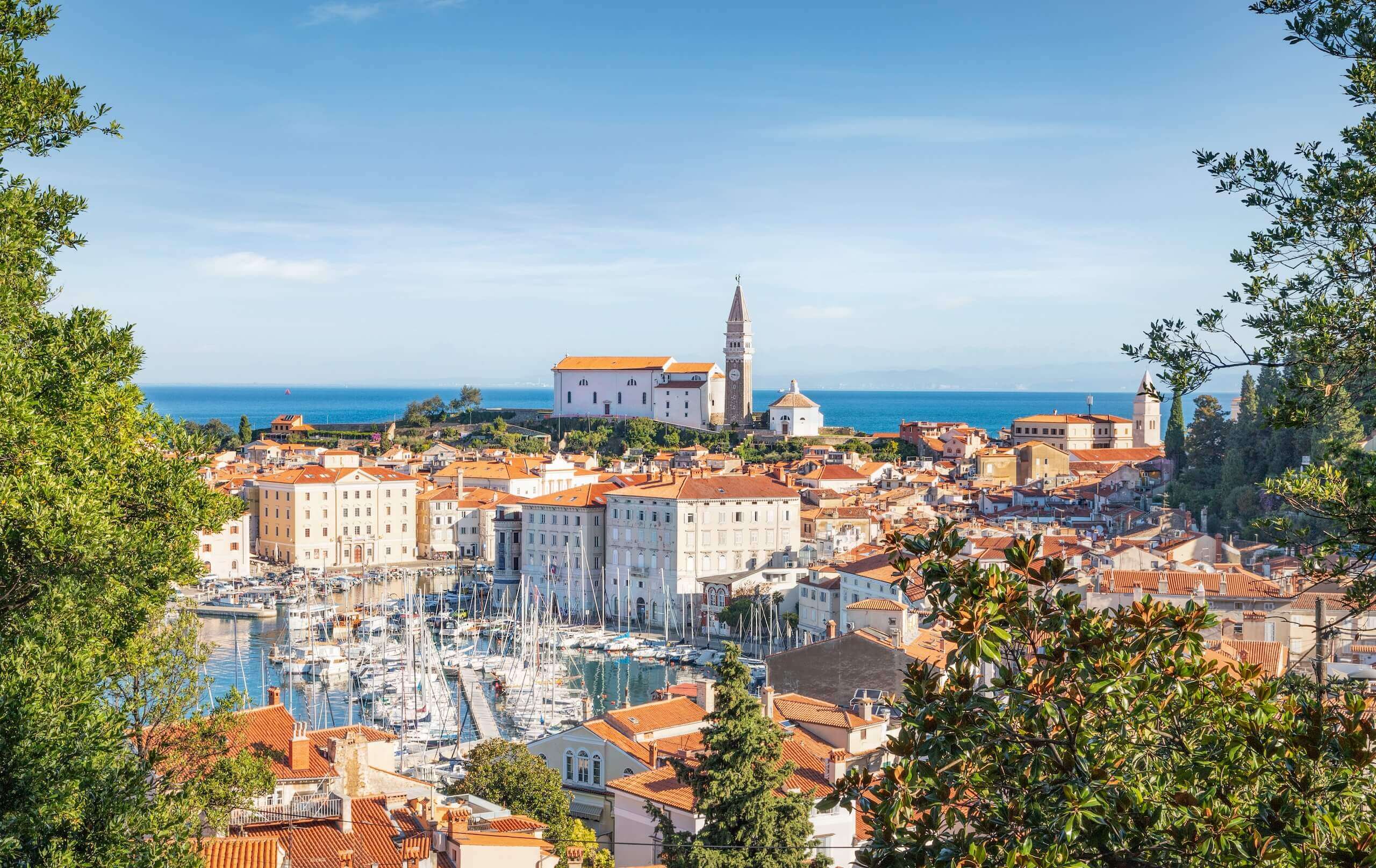 Panorama von Piran, Slowenien mit malerischem Hafen, roten Dächern und der Kirche St. Georg am blauen Meer.