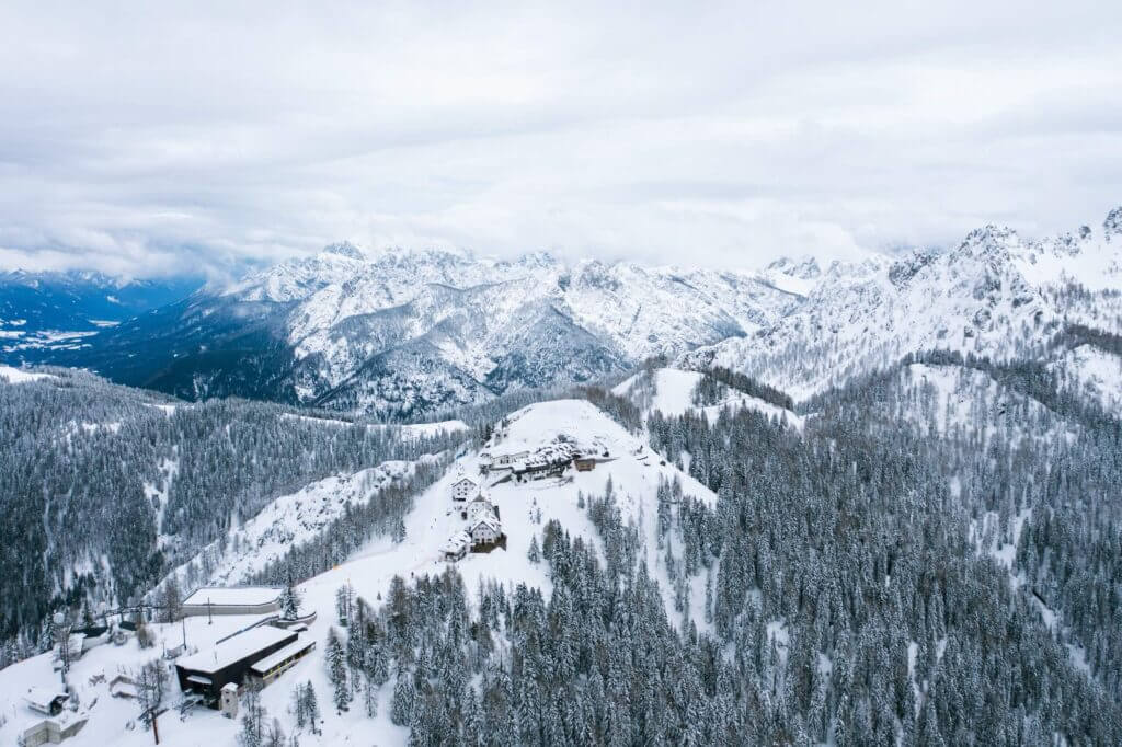 Verschneite Berglandschaft mit Wald und Hütten, umgeben von majestätischen Alpen im Winter. Ideal für Wintersport und Erholung.