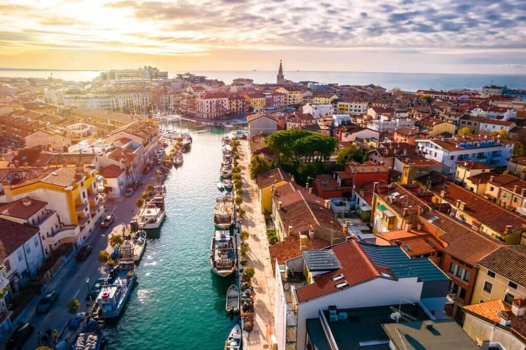 Luftaufnahme von Grado, Italien: malerische Kanäle, bunte Gebäude und ein atemberaubender Sonnenuntergang über dem Meer.