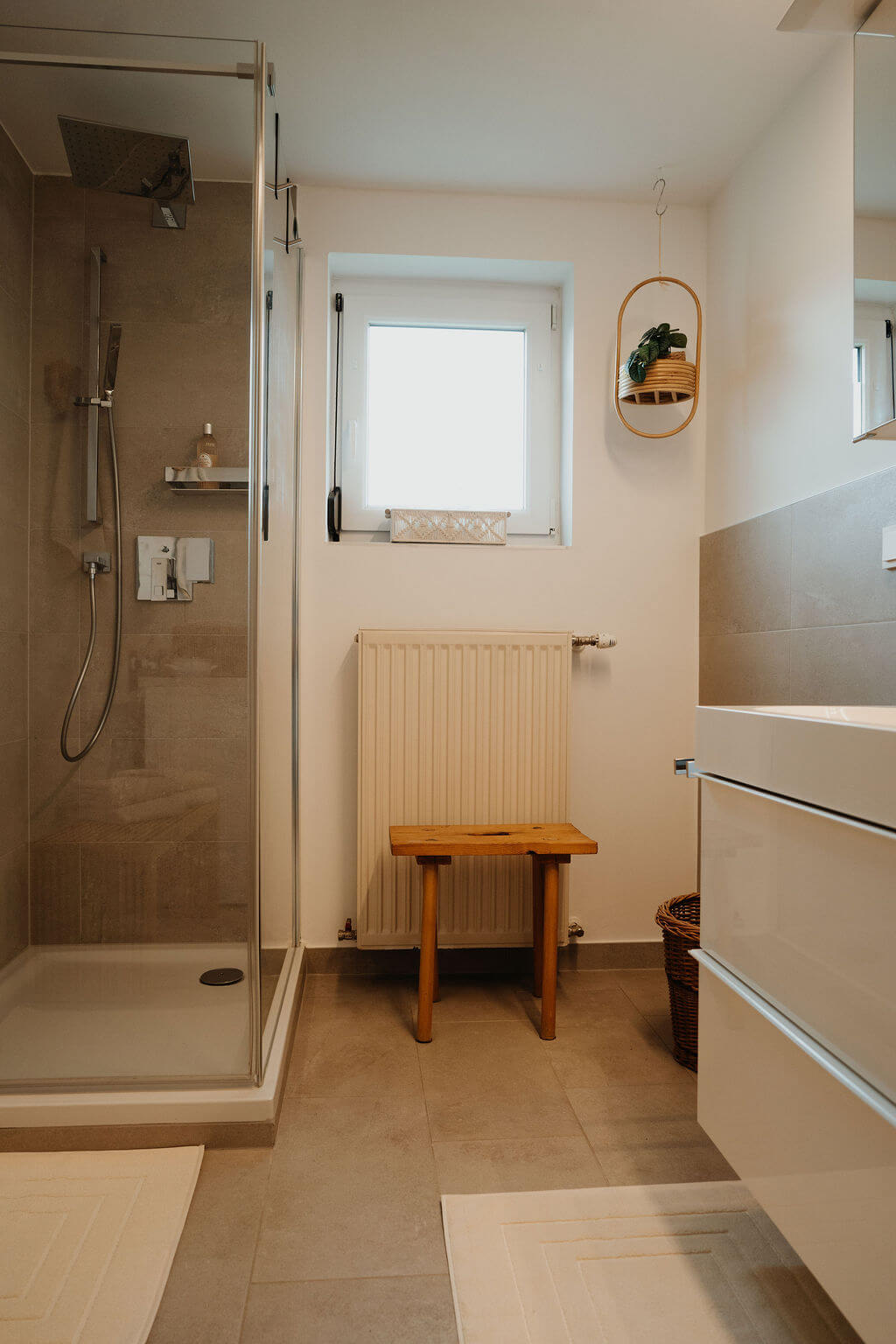 Modernes Badezimmer mit Dusche, Hocker und Hängepflanze für stilvolles, minimalistisches Design.
