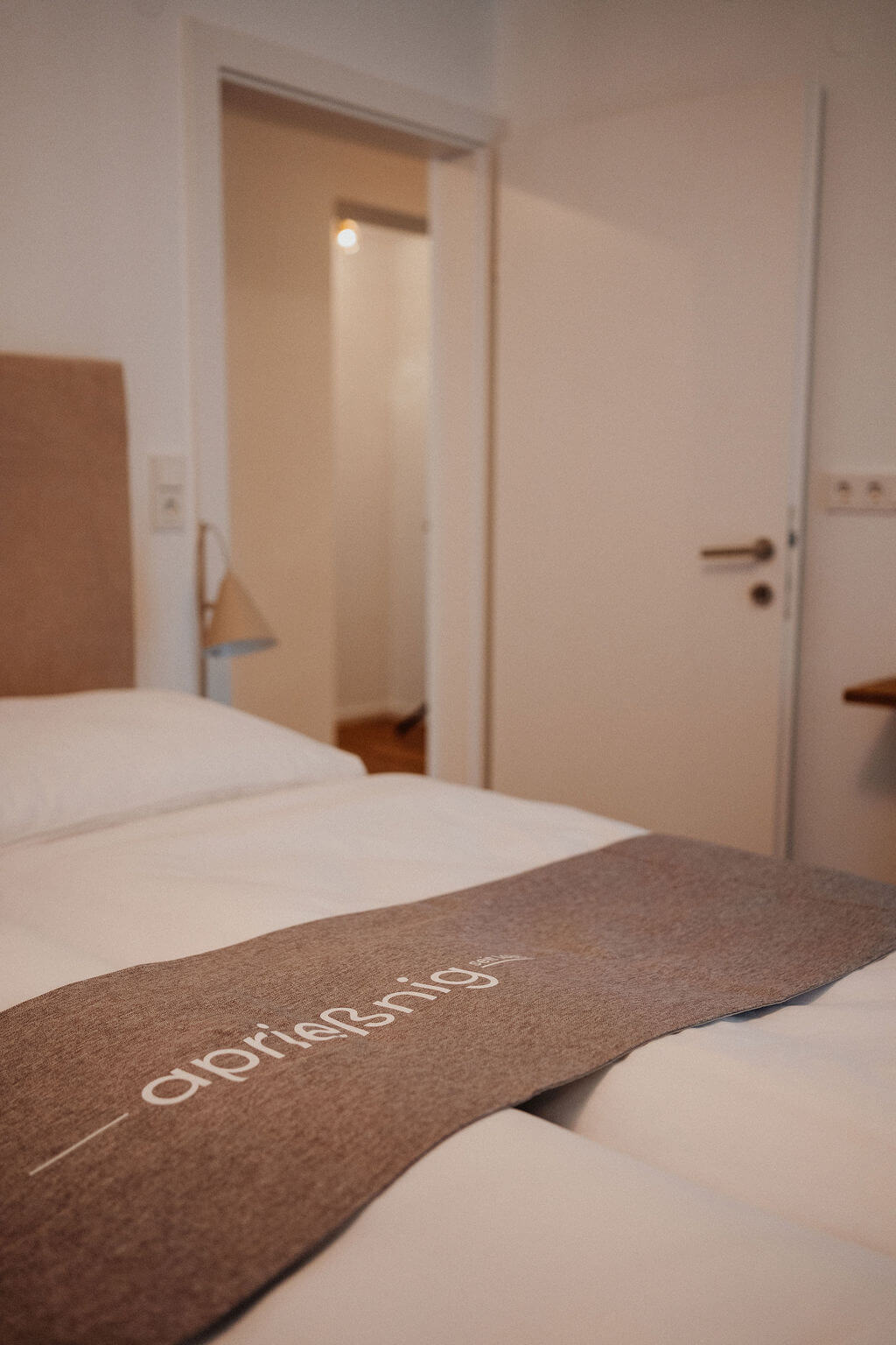 Einladendes Hotelzimmer mit elegantem Bett, weißer Bettwäsche und offenem Türblick.