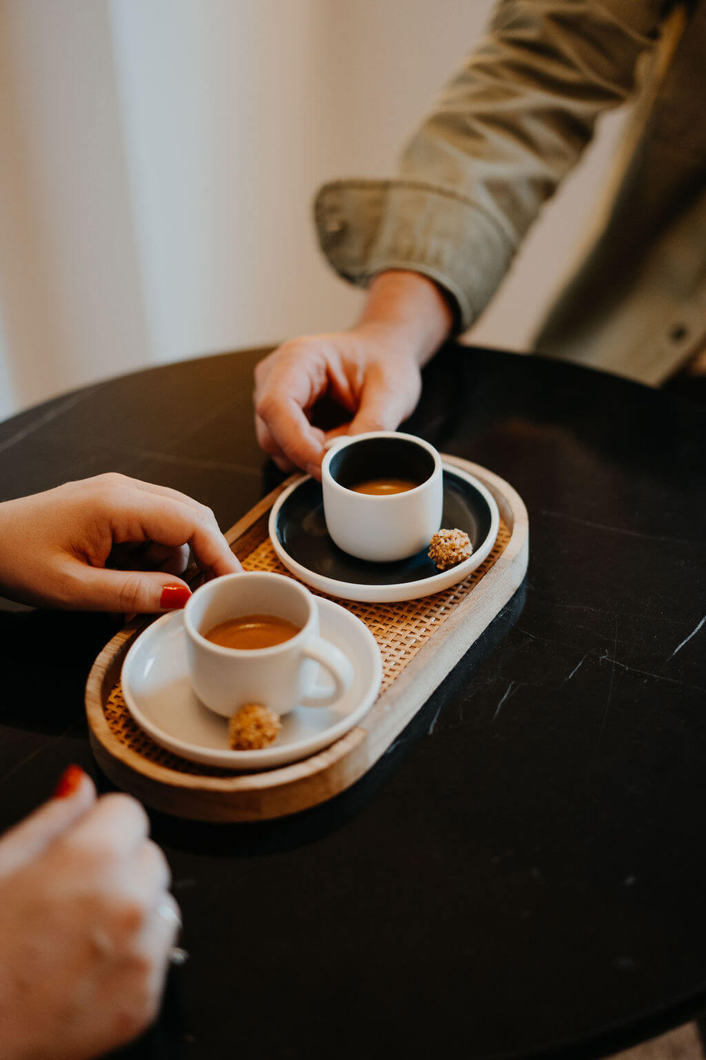 Zwei Personen genießen Espresso in weißen Tassen, serviert mit Keksen auf einem Tablett in einem Café.