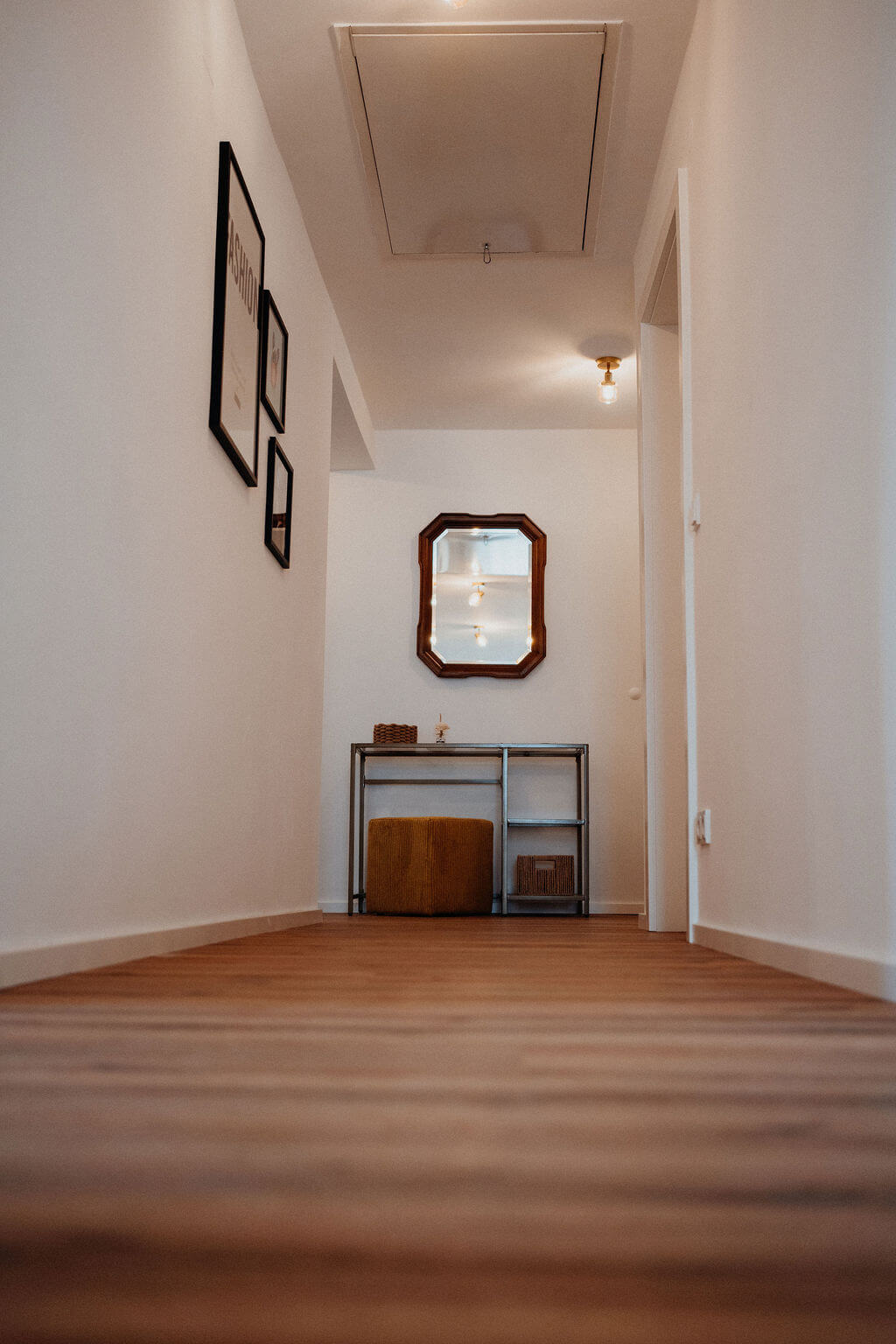Moderner Flur mit Holzboden, Wandbildern und Spiegel, darunter ein Tisch mit Dekor und Hocker.