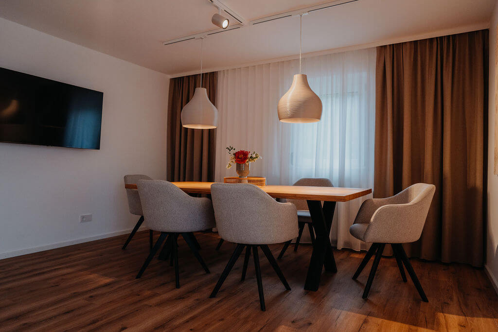 Moderner Essbereich mit Holztisch, grauen Stühlen, hängenden Lampen und einem Blumenstrauß in einem stilvollen Raum.