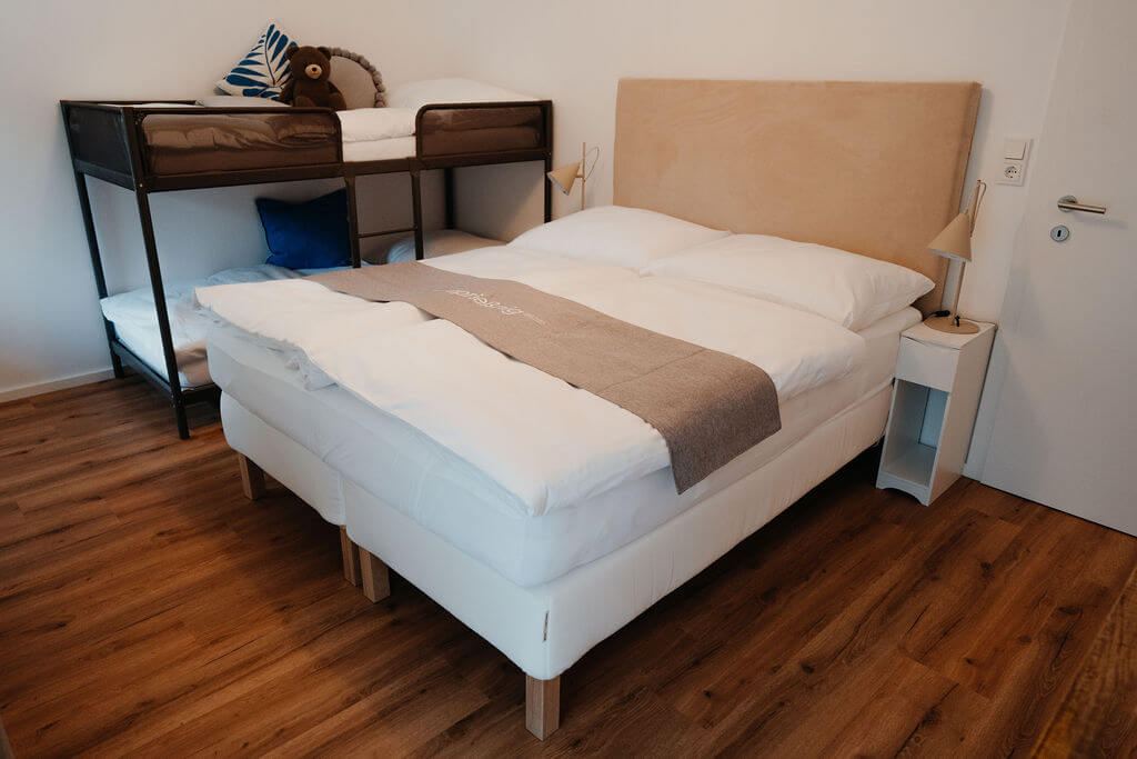 Modernes Schlafzimmer mit Etagenbett und Doppelbett auf Laminatboden, minimalistisch und gemütlich eingerichtet.