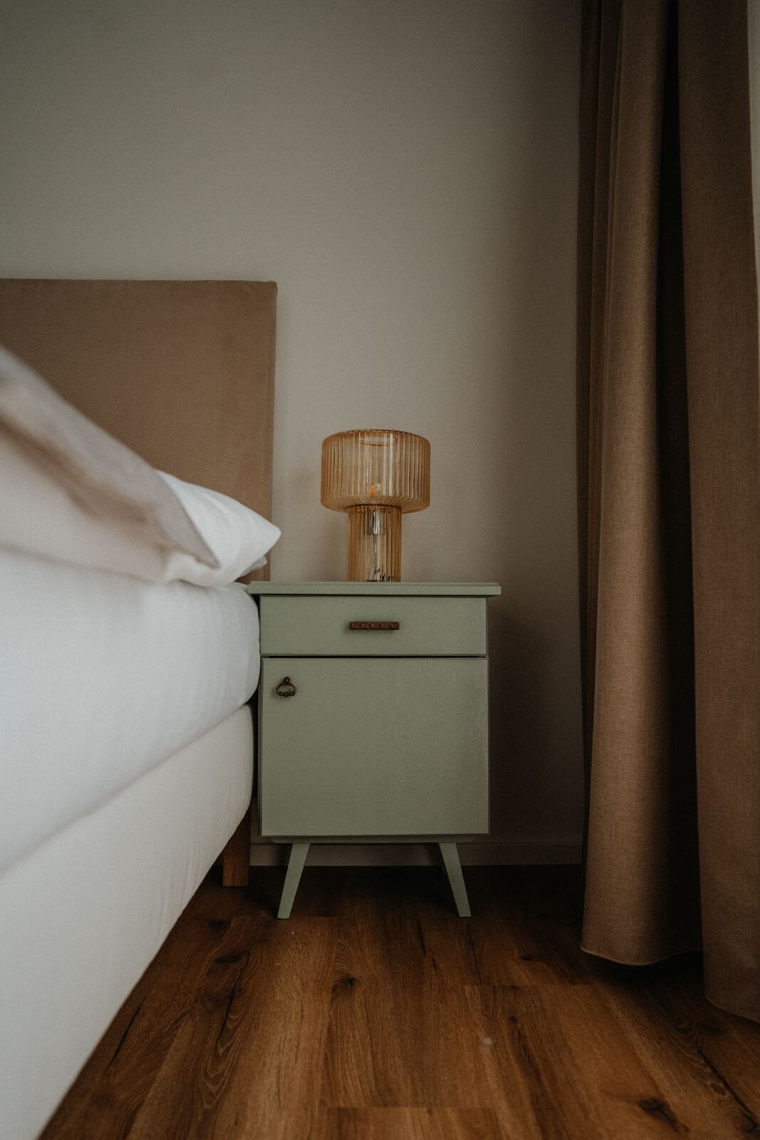 Nachttisch mit Retro-Lampe neben einem Bett auf Holzboden in einem stilvollen Schlafzimmer.