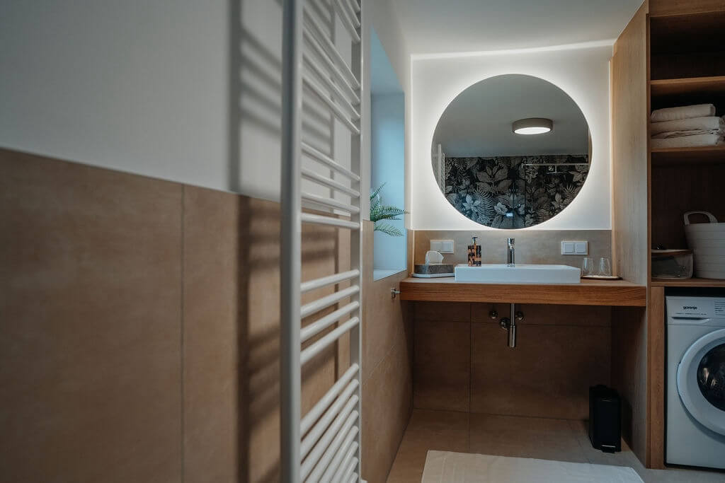 Modernes Badezimmer mit beleuchtetem rundem Spiegel, Waschbecken und elegantem Design. Ideal für stilvolle Inneneinrichtung.
