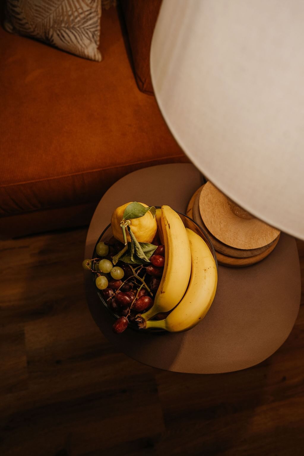 Obstschale mit Bananen, Trauben und einer Zitrone auf einem Tisch neben einer Lampe im gemütlichen Wohnzimmer.