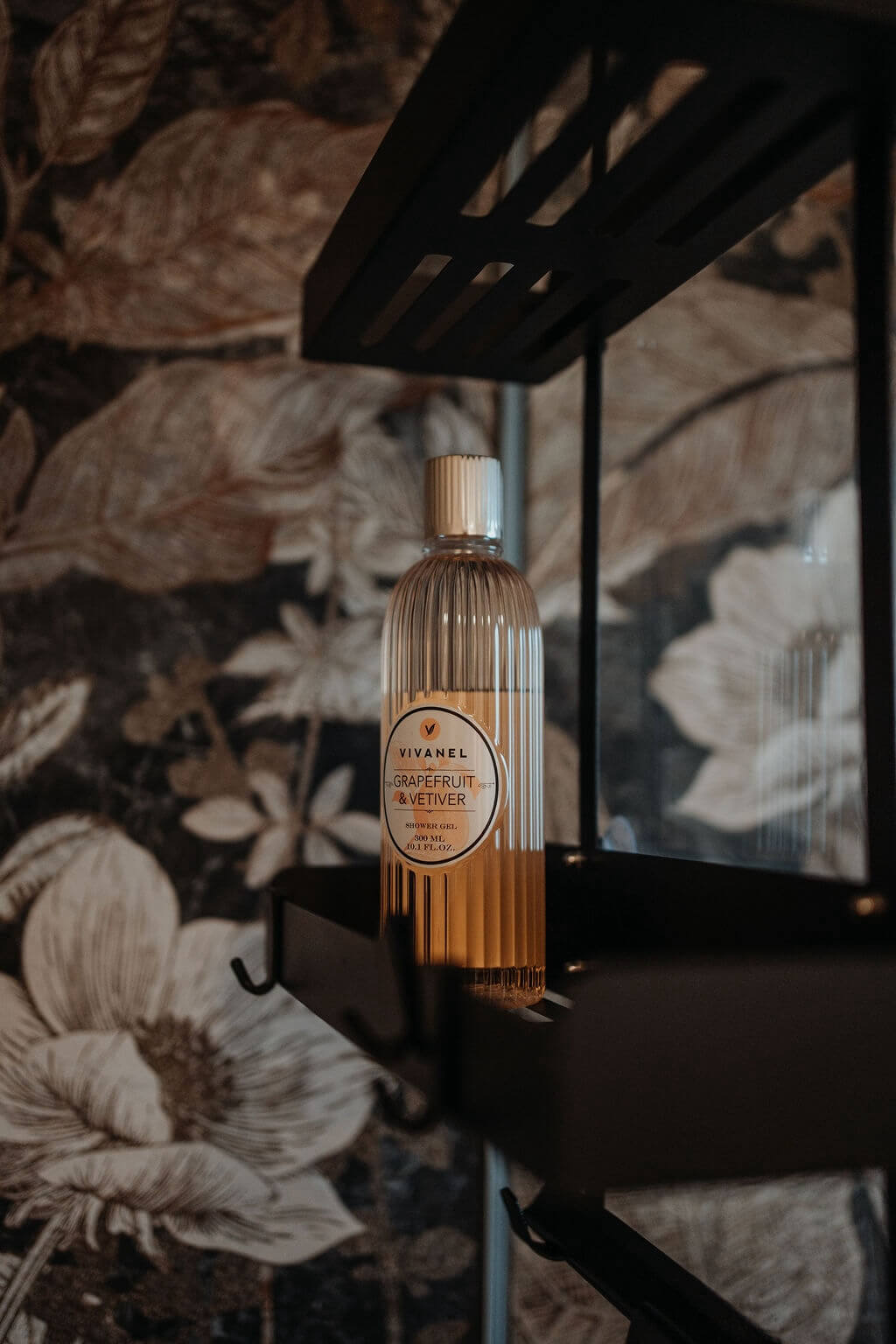 Duschgel-Flasche Grapefruit & Vetiver auf Regal, dezenter Hintergrund mit floralen Mustern.