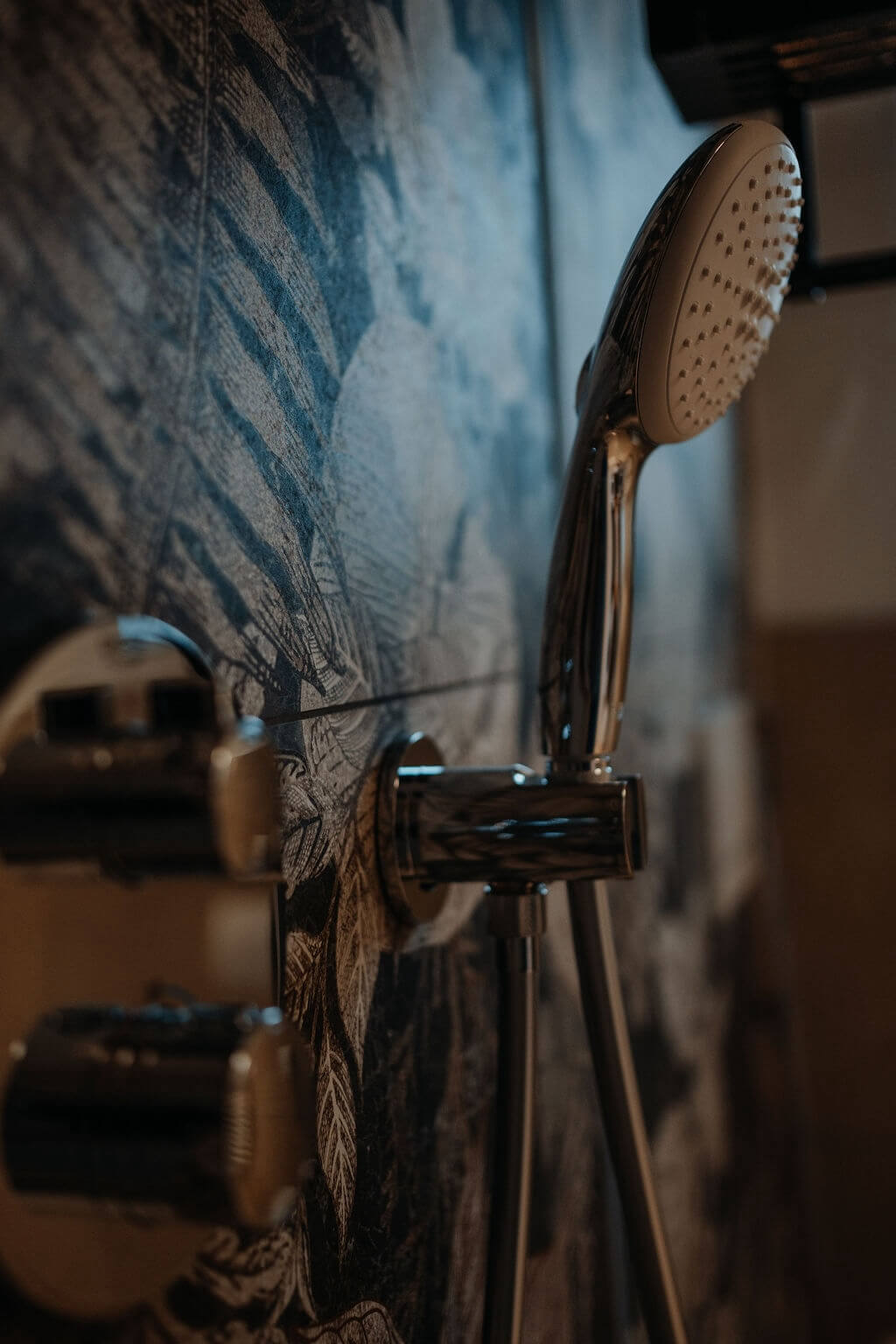 Moderne Handbrause vor floralem Wanddesign im Bad, beleuchtet für elegante Akzentuierung.
