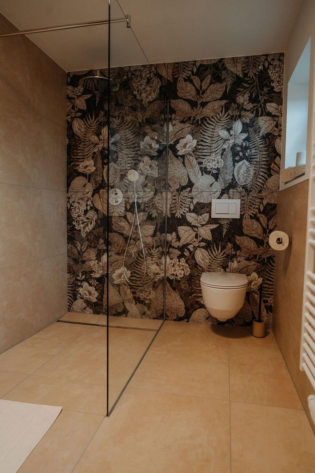 Moderner Duschbereich mit floralem Wanddesign, Glasabtrennung und beigefarbenen Fliesen im stilvollen Badezimmer.