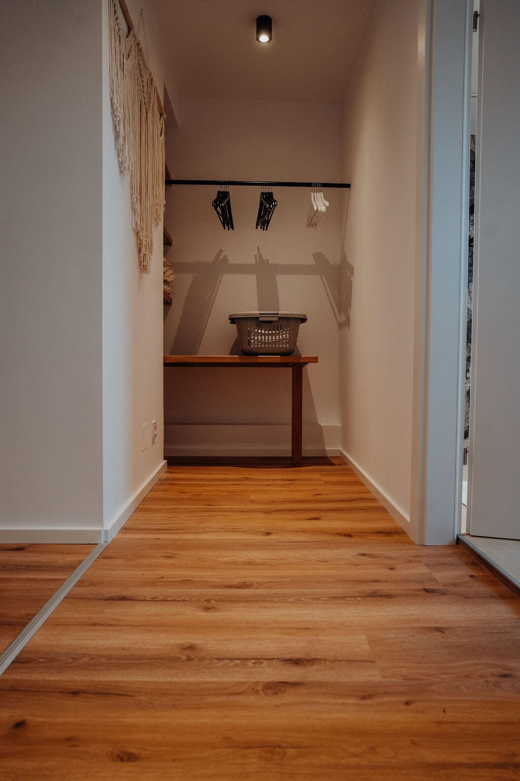 Minimalistischer Kleiderschrank mit Kleiderstange, Holzbank und Wäschekorb auf Holzfußboden. Moderne Aufbewahrungslösung.