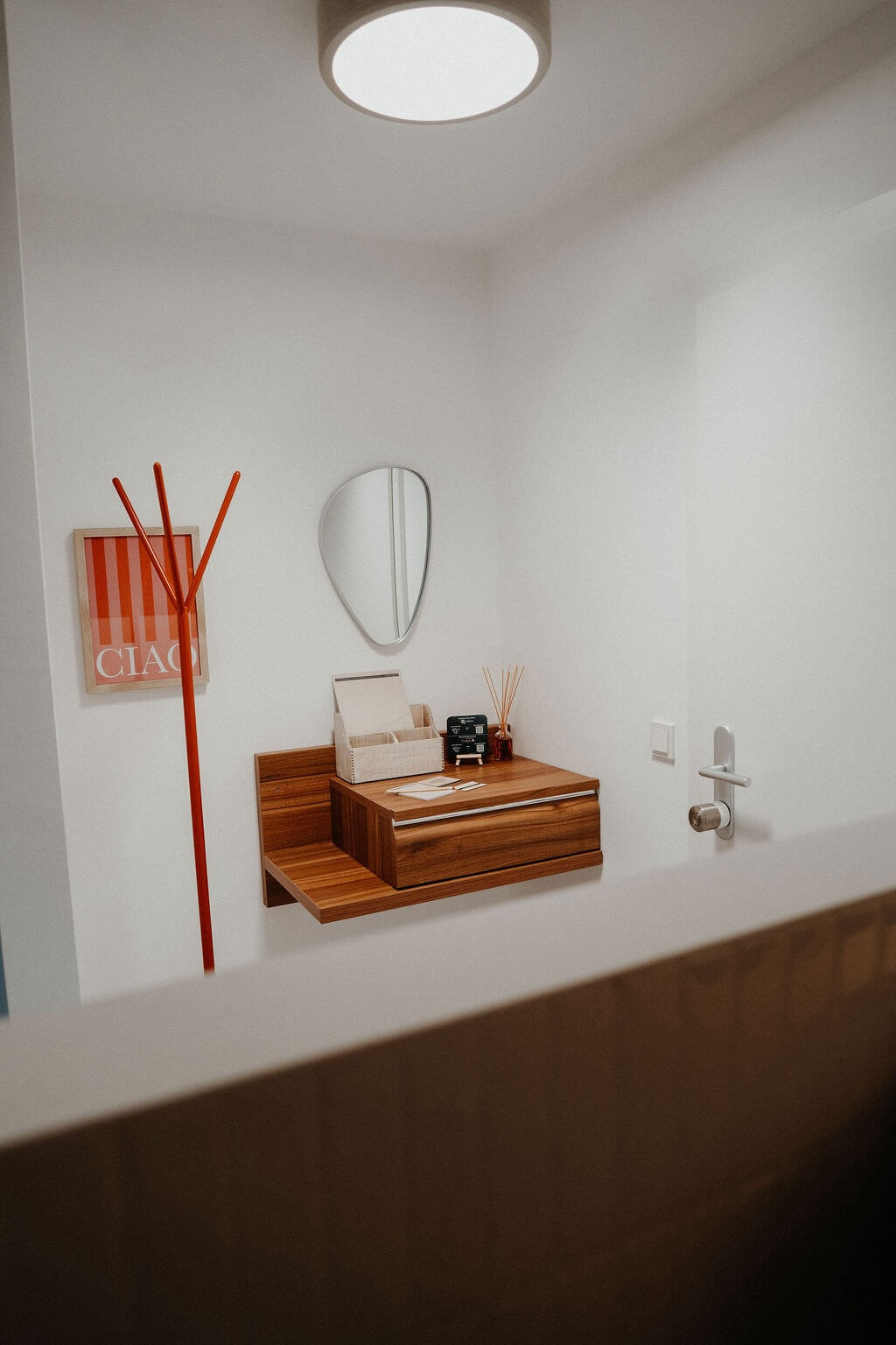 Moderner Eingangsbereich mit Holz-Regal, rotem Kleiderständer und Wandspiegel in minimalistischem Design.