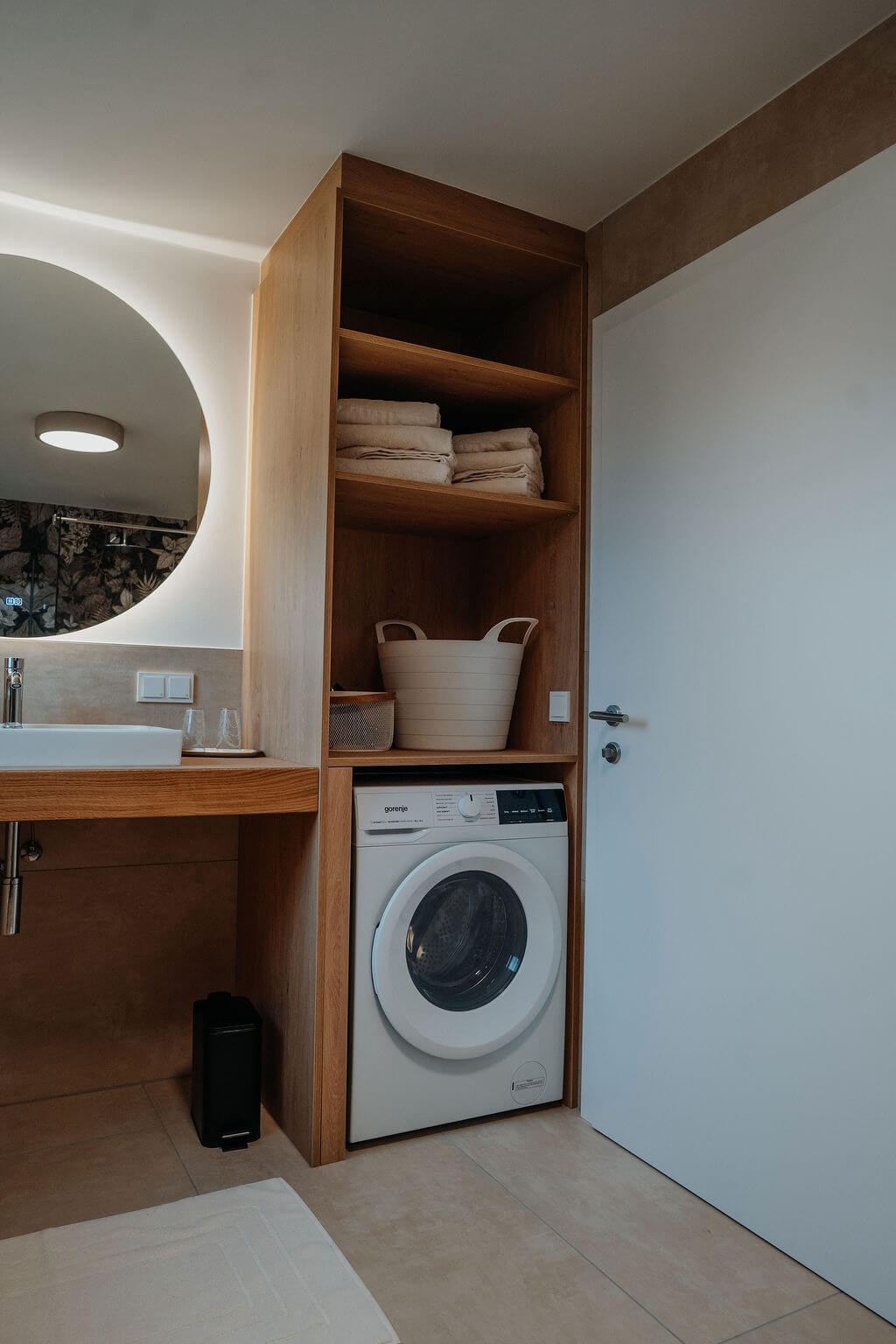 Moderner Waschküchenbereich mit Waschmaschine und Holzregalen, ideal für kleine Badezimmer.